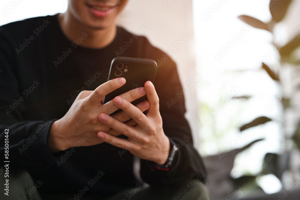 Smiling young asian man texting message, chatting friend on smart phone. People, technology and communication concept.