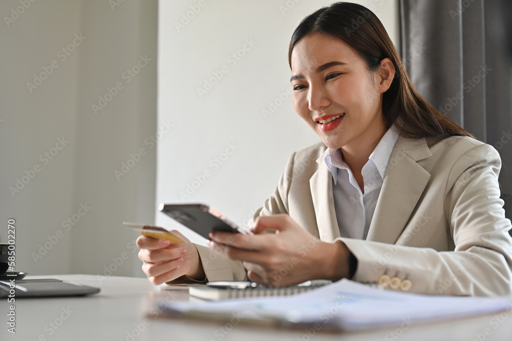 Smiling woman holding mobile phone and credit card, online shopping on internet, enjoy easy fast secure transferring money in mobile banking app. Smiling woman holding mobile phone and credit card, online shopping on internet, enjoy easy fast secure transferring money in mobile banking app.