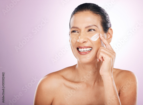 Face smile, cream and skincare of woman in studio isolated on a purple background. Mature, thinking and happy female model apply dermatology lotion, creme and moisturizer cosmetics for healthy skin.
