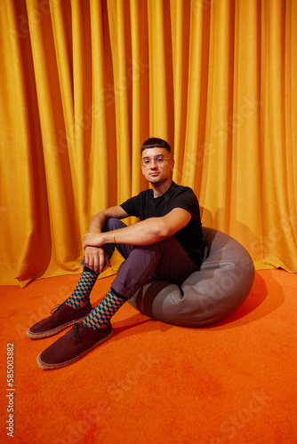 Confident guy sitting on Sacco bag in orange room