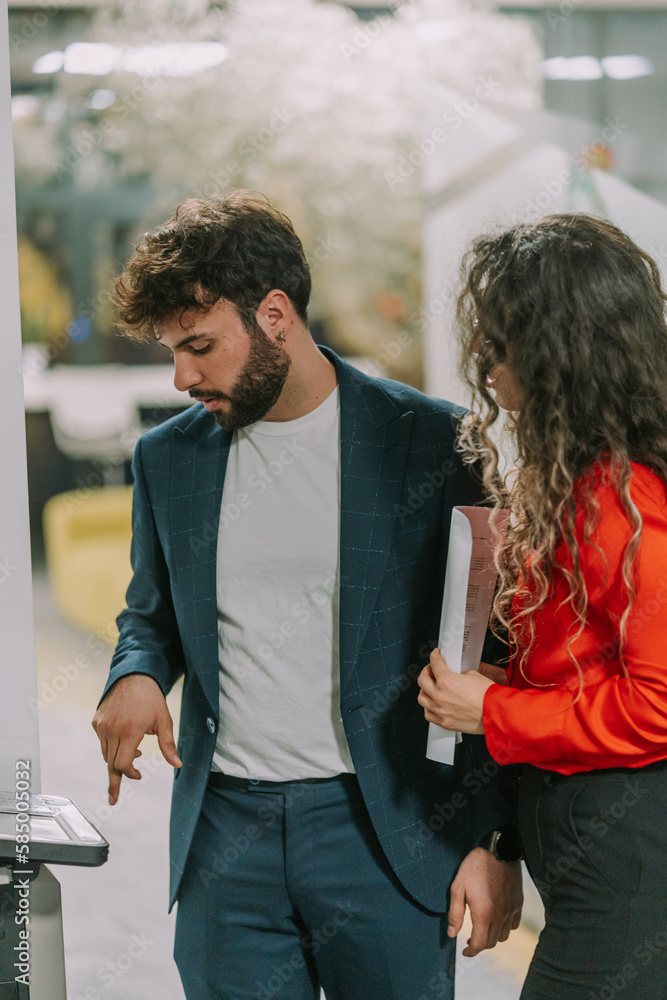 Fototapeta premium Handsome male business person printing some documents at the office while his girlfriend is standing next to him