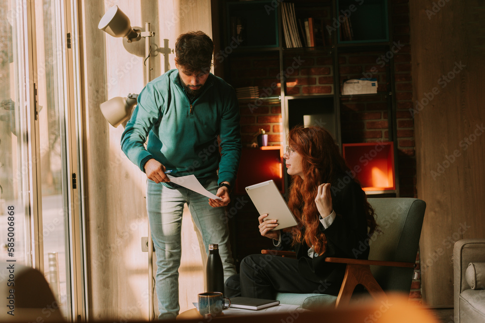 Ginger businesswoman trying to help her male coworker. She is looking at his document and explaining to him Ginger businesswoman trying to help her male coworker. She is looking at his document and explaining to him