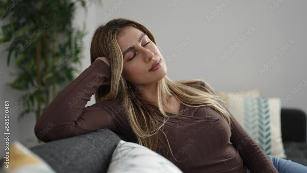 Young blonde woman relaxed with hands on head sitting on sofa at home Young blonde woman relaxed with hands on head sitting on sofa at home
