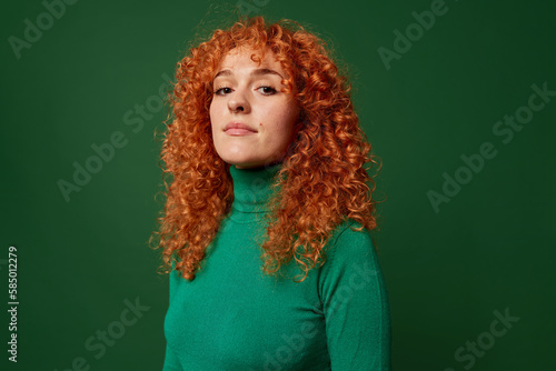 Self assured young ginger woman on green background