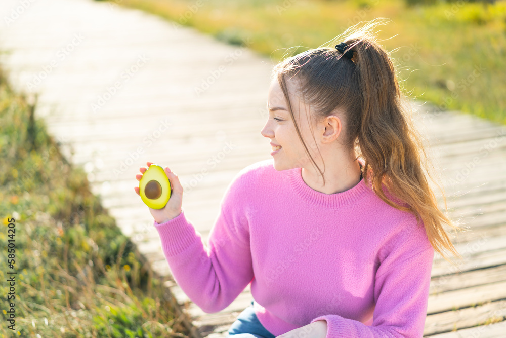 Young pretty girl holding an avocado at outdoors with happy expression Young pretty girl holding an avocado at outdoors with happy expression