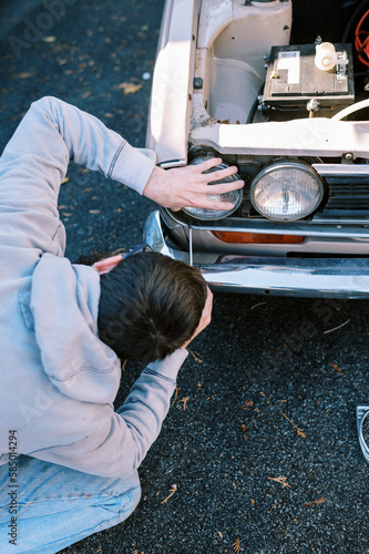 Millennial man replacing headlights in classic station wagon photo