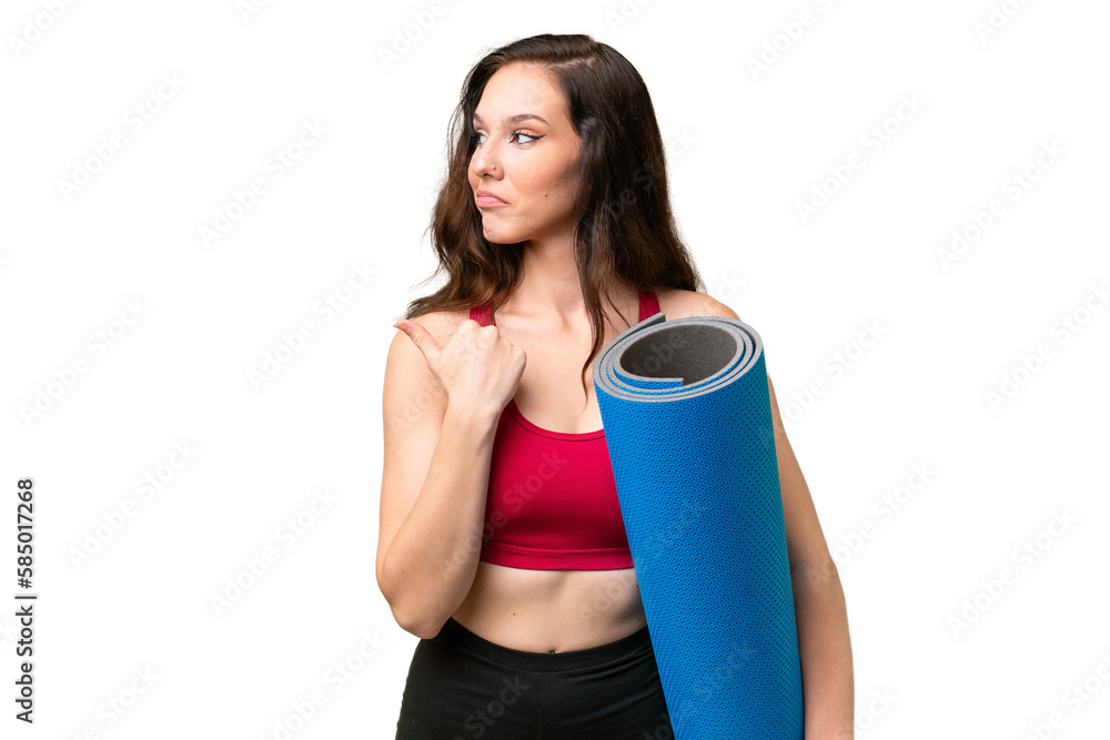 Young sport woman going to yoga classes while holding a mat over isolated background pointing to the side to present a product Young sport woman going to yoga classes while holding a mat over isolated background pointing to the side to present a product