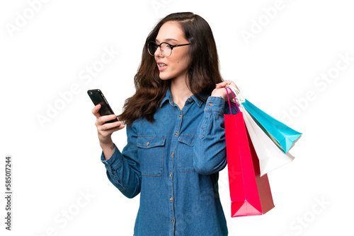 Young caucasian woman over isolated background holding shopping bags and writing a message with her cell phone to a friend