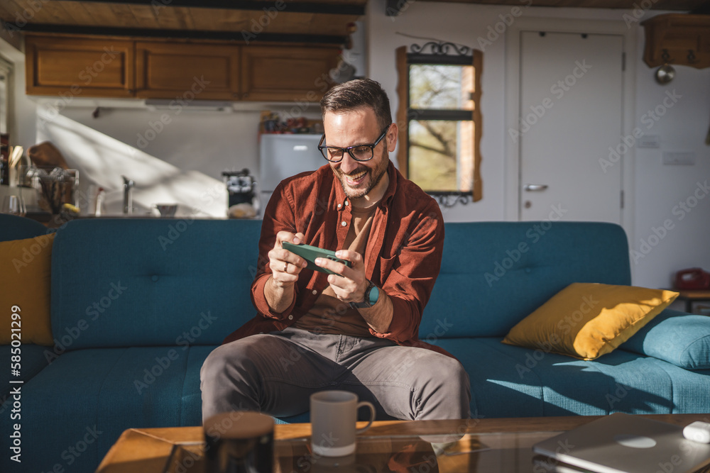 caucasian man sit at home play video games on smartphone mobile phone