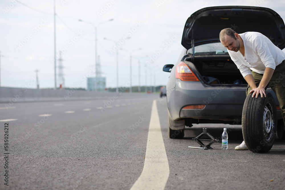 Replacing the wheel of a car on the road. A man doing tire work on the sidelines.