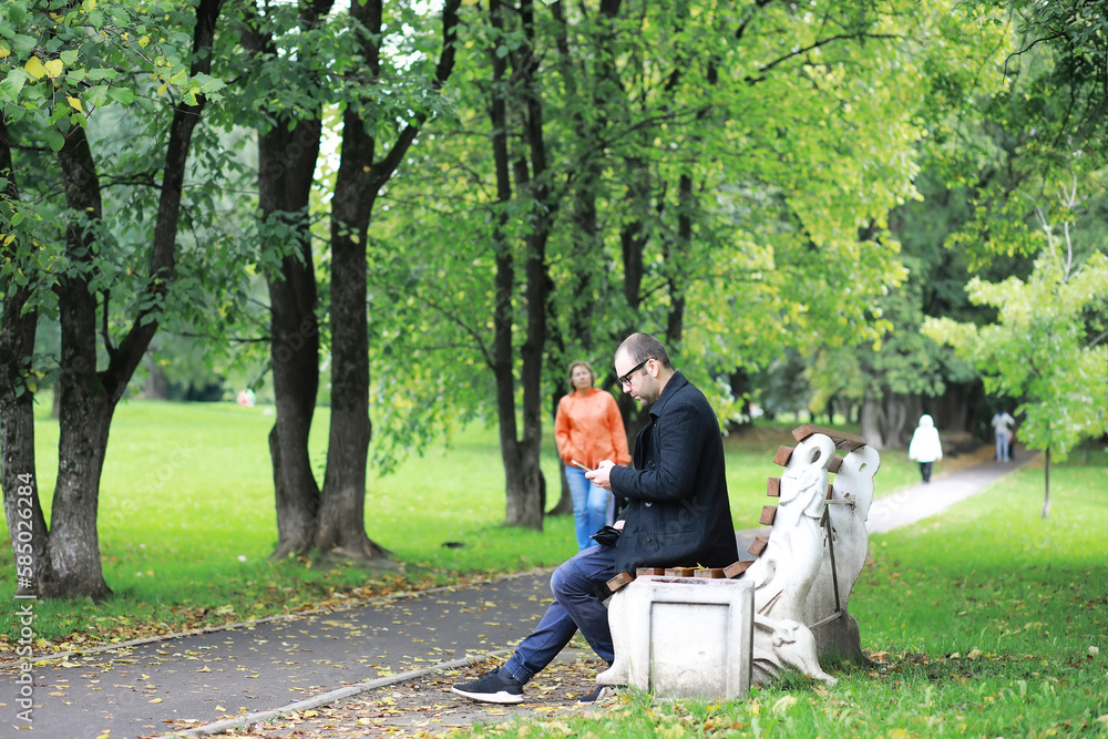 Fototapeta premium A young man in glasses walks in the park with an umbrella during the rain.