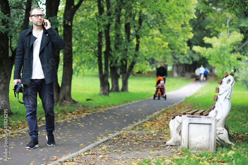Photography A young man in glasses walks in the park with an umbrella during the rain