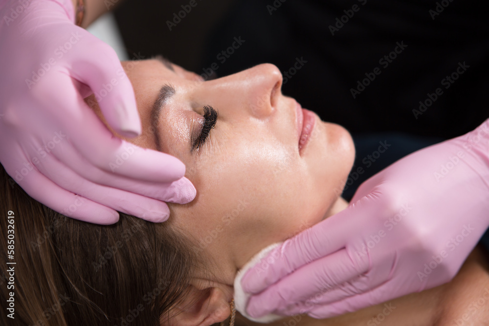 Beautician in a beauty salon holds a cotton pad with which he cleans the face of a woman. Skin care and rejuvenation procedures. Beautician in a beauty salon holds a cotton pad with which he cleans the face of a woman. Skin care and rejuvenation procedures.