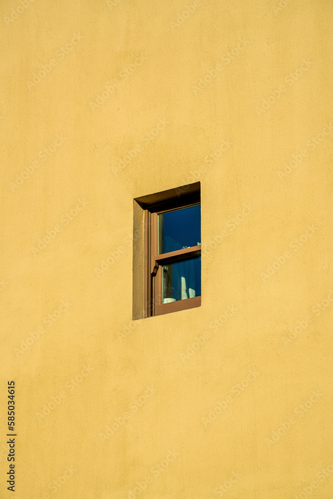 Small exterior window in downtown building with brown or beige cement stucco facade in downtown urban area of city Small exterior window in downtown building with brown or beige cement stucco facade in downtown urban area of city