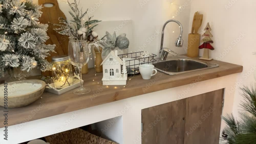 Light rustic style kitchen, decorated for Christmas with New Year's decor and a garland, rustic kitchen interior for Christmas, dishes, sink, candlestick house on Christmas morning Light rustic style kitchen, decorated for Christmas with New Year's decor and a garland, rustic kitchen interior for Christmas, dishes, sink, candlestick house on Christmas morning
