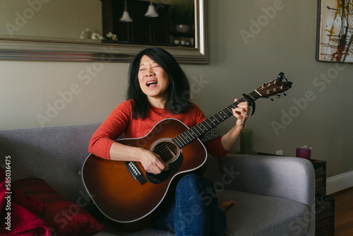 happy woman singing and playing guitar in her home photo