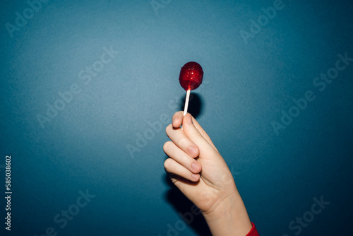hand holding red lollipop agains blue background 