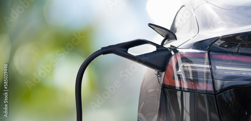 Close up of electric car inlet with a connected charging cable on a green background
