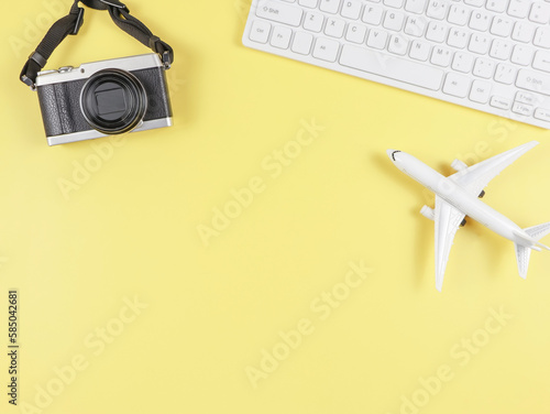 flat lay of airplane model, computer keyboard, and digital camera with copy space on yellow background, business and traveling concept.