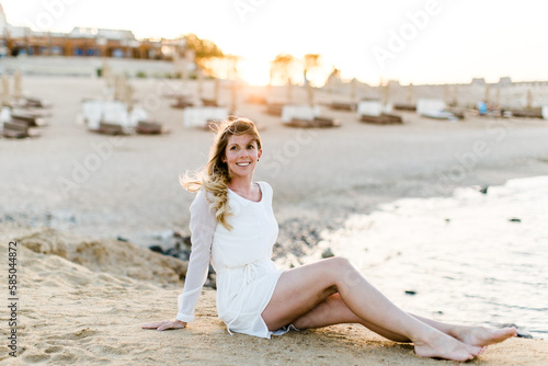 Frau im wei  en Kleid sitzt am Strand