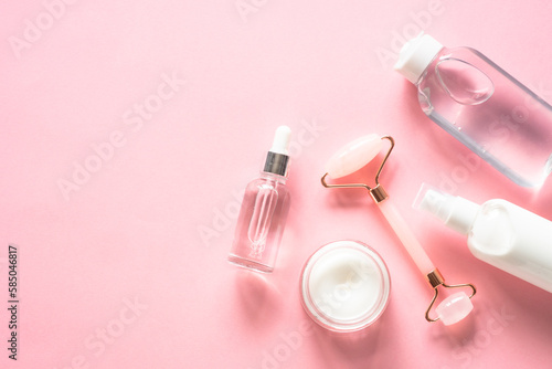 Skin care concept. Jade roller, cream and serum bottle on pink. Flat lay image with copy space.