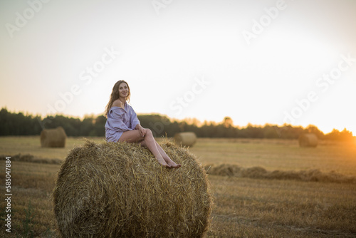 a happy girl with long hair sits on a haystack in a field at sunset and enjoys nature, loneliness and freedom.