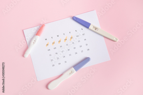 Flat lay Inkjet pregnancy test kits on a white calendar with marked dates in last menstruation, pink background. Calculation of ovulation day. Planning maternity. Gynecology and women's health concept photo