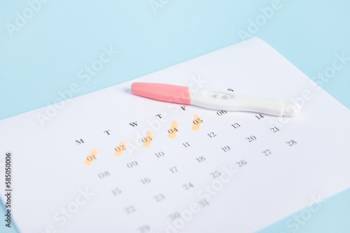 Selective focus. Pregnancy inkjet test and a calendar with dates of the last menstruation marked on blue color background. Women's health. Ovulation date calculation. Planning pregnancy and maternity photo