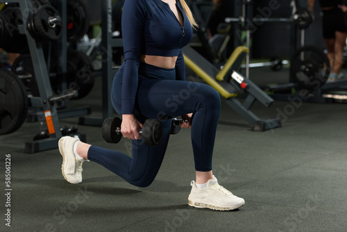 Photo of sporty caucasian woman squatting with small weights. wearing blue leggins and long sleeve top.