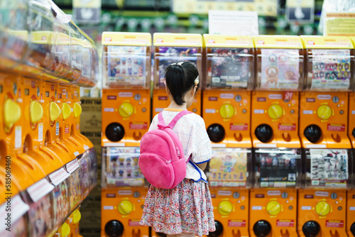 Behind of young Asian girl concentrate on picking the toy out from Gachapon machine in mall, tourist attraction, vacation activity. kid leisure. photo