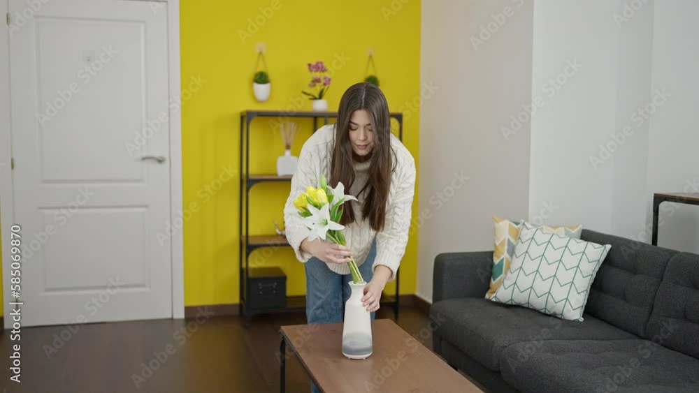 Young beautiful hispanic woman putting flowers on pot at home Young beautiful hispanic woman putting flowers on pot at home