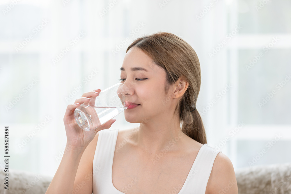 Healthy wellness lifestyle concept. Beautiful Asian young woman drinking refreshing water from a glass during read book relax at home. Detox and self-care. Healthy wellness lifestyle concept. Beautiful Asian young woman drinking refreshing water from a glass during read book relax at home. Detox and self-care.