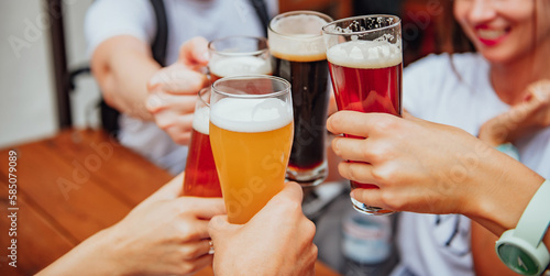 A company of cheerful young multi-ethnic friends clink glasses with different beers on a restaurant terrace on a summer day. a company of young people clink glasses with different types of beer. 