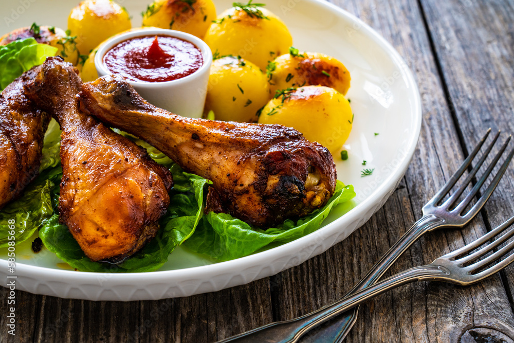 Barbecue chicken drumsticks with fried potatoes, lettuce and ketchup on wooden table
