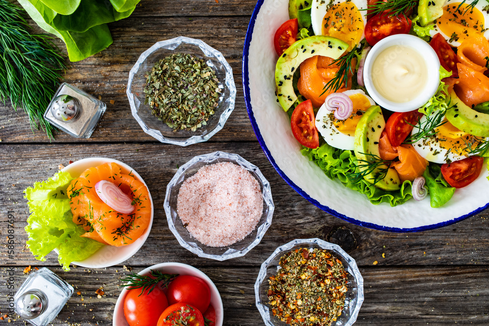 Salmon salad - smoked salmon, hard boiled eggs, avocado and leafy greens on wooden table
