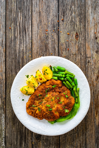 Breaded fried pork chop with green beans and potatoes on wooden table
