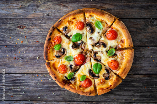 Circle vegetarian pizza with mozzarella cheese  mushrooms and tomatoes on wooden table 