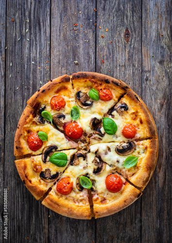 Circle vegetarian pizza with mozzarella cheese, mushrooms and tomatoes on wooden table 