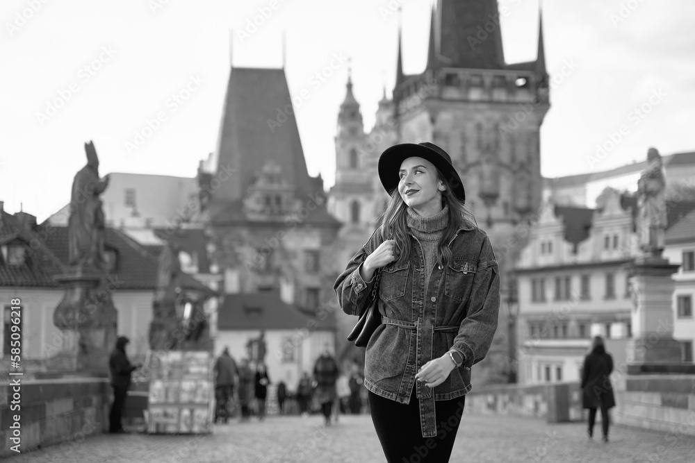 Female traveller tourist on the Charles Bridge in Prague, Czezh Repubic. Stylish beautiful young woman earing black hat. Elegant retro black and white portrait.