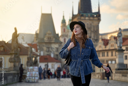 Female traveller tourist on the Charles Bridge in Prague, Czezh Repubic. Stylish beautiful young woman earing black hat. Elegant retro lady fine art portrait. © berezko