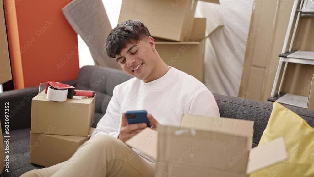 Young hispanic man using smartphone sitting on sofa at new home Young hispanic man using smartphone sitting on sofa at new home
