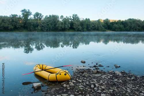 Packrafting concept with yellow packraft boat on a calm sunrise river with morning fog. Active lifestile background