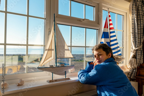 A woman in a sweater sitting near the window in a classic old hotel room with a sea view after packing a suitcase #585099451