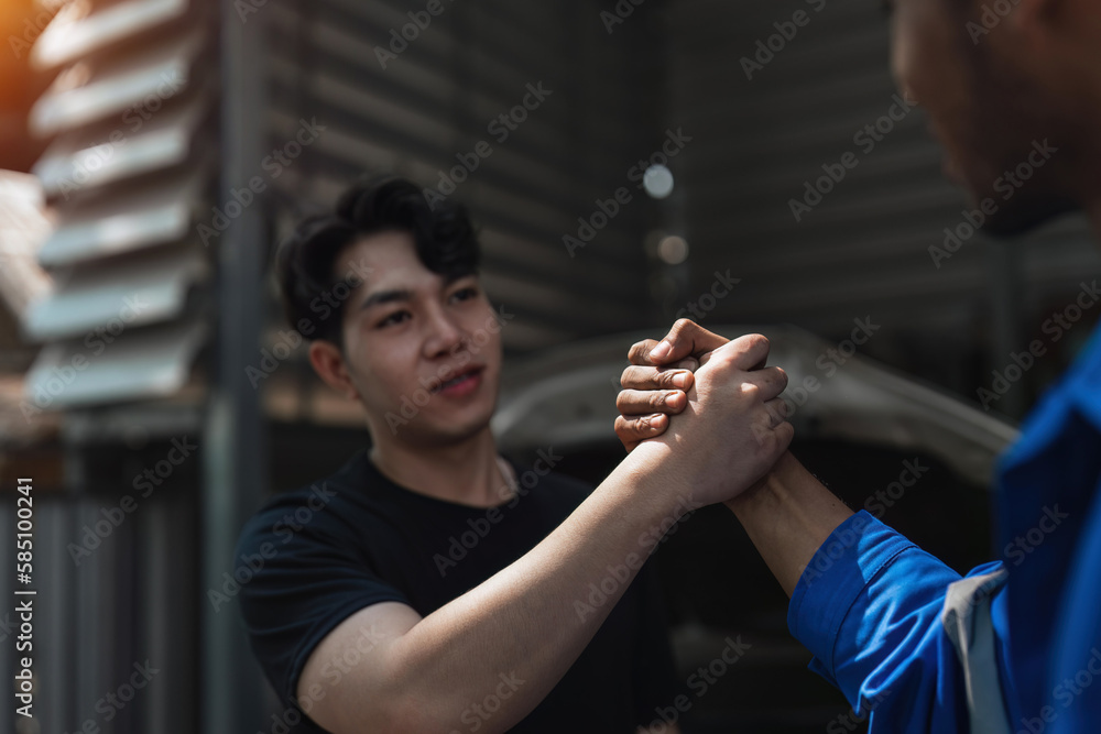Young man client shaking hands with auto mechanic in red uniform having a deal at the car service Young man client shaking hands with auto mechanic in red uniform having a deal at the car service