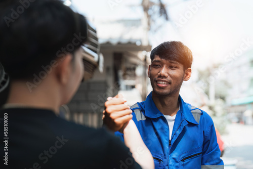 Young man client shaking hands with auto mechanic in red uniform having a deal at the car service