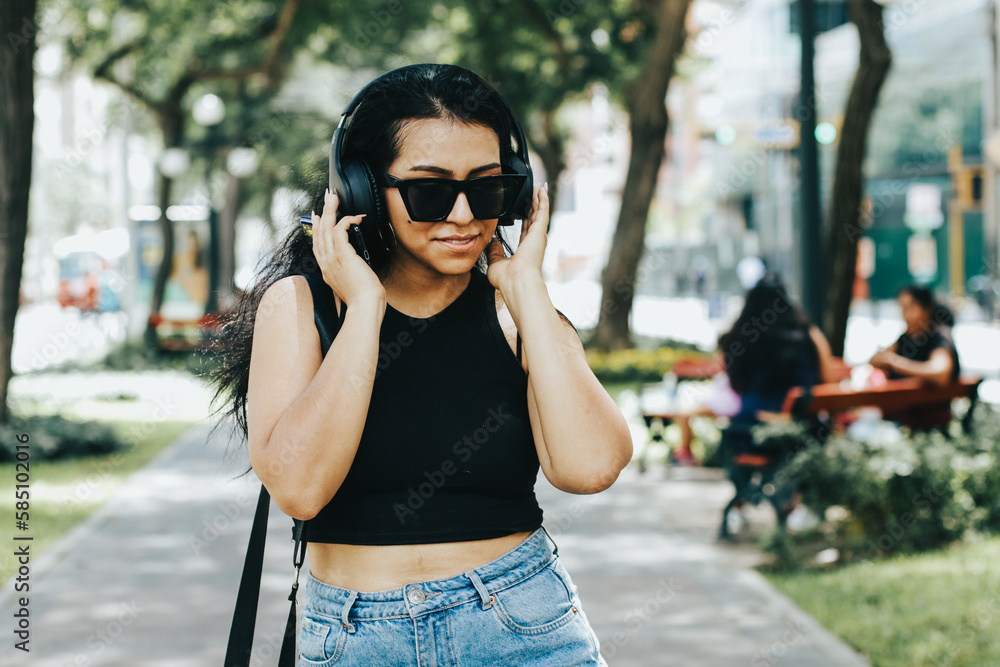 Photo of a woman listening to music with wireless headphones while wearing sunglasses. Lifestyle concept.