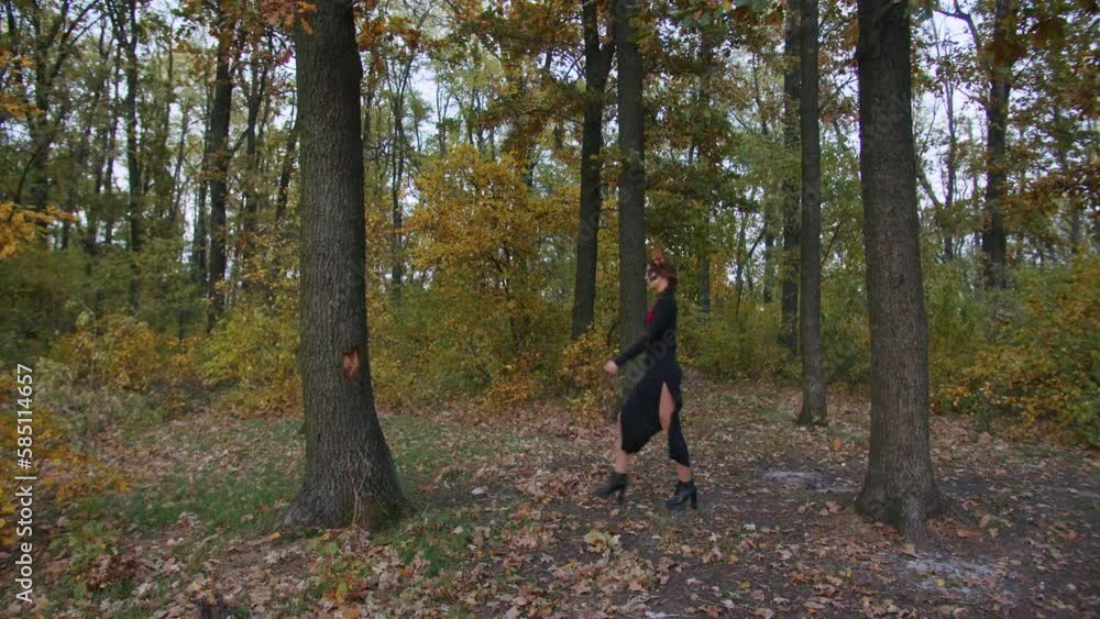 A young woman with Santa Muerte make-up dressed in a black dress of death walks against the backdrop of autumn leaves in the forest during sunset. Day of the Dead or Halloween concept. A young woman with Santa Muerte make-up dressed in a black dress of death walks against the backdrop of autumn leaves in the forest during sunset. Day of the Dead or Halloween concept.