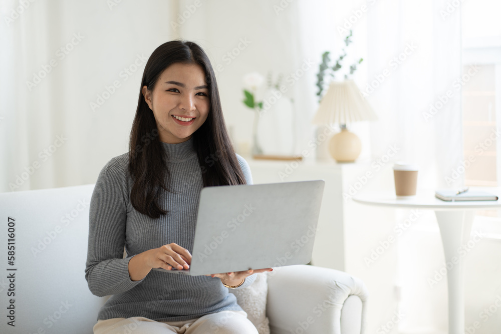 Young beautiful Asian woman using laptop computer while sitting on the sofa at her living room. Young beautiful Asian woman using laptop computer while sitting on the sofa at her living room.