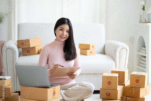 Young SME start up business woman writing down information in her room full of parcel boxes.