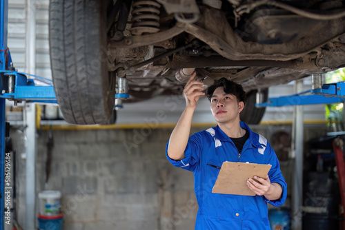 Vehicle service maintenance asian man checking under car condition in garage. Automotive mechanic maintenance checklist document. Car repair service concept